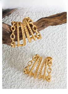 Macro detail of triple-layer C-shaped gold-plated steel earrings on a wooden branch