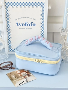 Close-up of quilted blue makeup bag featuring yellow zipper and pink embroidered handle
