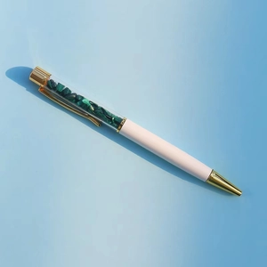 Dettaglio di una penna a sfera creativa con pietre di cristallo verdi e oro rosa