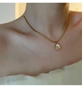 Close-up of a gold-toned avocado shell pendant necklace worn on a woman's collarbone