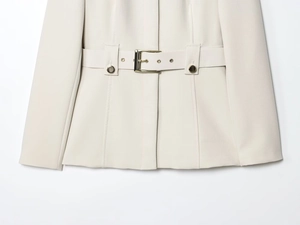 Détail d'un blazer crème avec tissu en sergé texturé et boucle de ceinture métallique