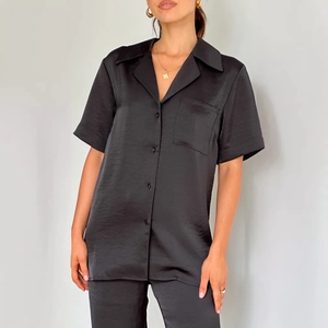 Detail of black satin pajamas featuring a notched lapel, front pocket and smooth texture