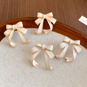 Elegant cream enamel bow stud earrings with gold trim on a decorative wooden display