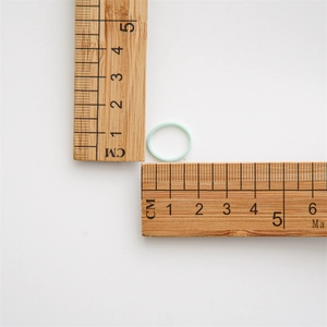 Macro detail of a 1.5cm light green elastic hair tie next to a wooden measuring scale