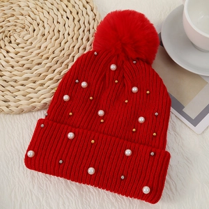 Close-up of red knit beanie with soft faux fur pompom and white pearl embellishments