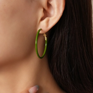 Dettaglio di un orecchino rotondo verde con chiusura in metallo indossato da una modella