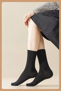 Close-up of elegant black mid-calf socks in combed cotton on a model in a warm room