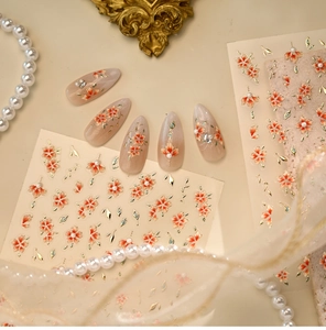 Detail of floral nail stickers with gold edges on pink base featuring pearls and rhinestones