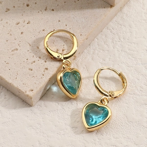 Vue détaillée de boucles d'oreilles cœur dorées avec cristaux bleu clair sur pierre