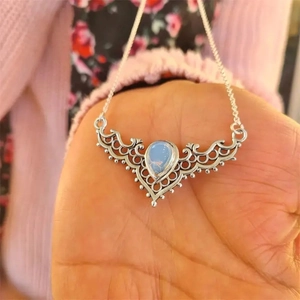 Silver antler necklace with hollow moonstone pendant shown on a hand against fabric