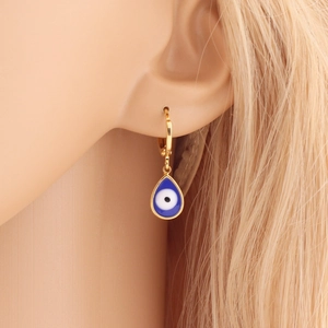 Close-up of a gold teardrop earring with a blue evil eye charm worn by a model