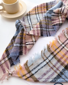 Flat lay of pink and blue plaid scarf with fringes next to a ceramic cup on white surface