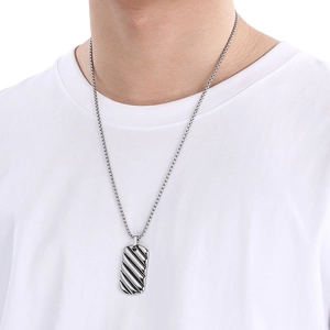 Close-up of a silver rectangular textured pendant on a stainless steel chain worn by a man