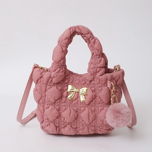 Détail du sac à main en nylon rose matelassé avec nœud doré et pendentif pompon doux