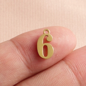 Golden stainless steel number 6 pendant charm for necklaces shown on a fingertip