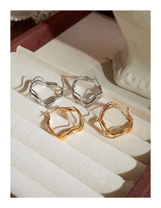 Macro view of minimalist irregular wavy hoop earrings in gold and silver metal finishes
