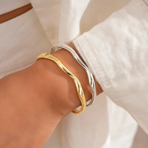 Detail of 18k gold and silver irregular wave bracelets worn on a model's wrist