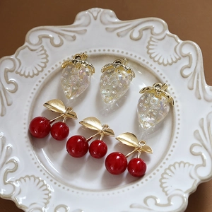 Close-up of translucent strawberry and red cherry pendants on a vintage ceramic plate
