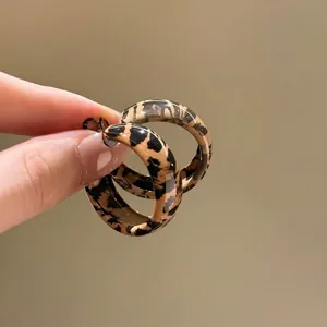 Close-up of small C-shaped leopard print earrings in brown and black resin finish