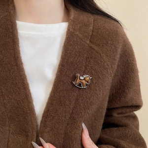 Close-up of a brown enamel rocking horse brooch with diamonds on a cozy cardigan