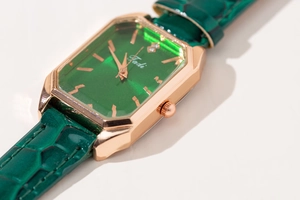 Macro shot of rose gold rectangular watch case with emerald green sunray dial and strap