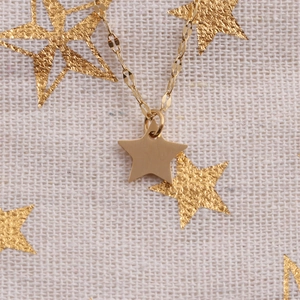 Close-up of golden star pendant necklace with fine metal chain on textured fabric