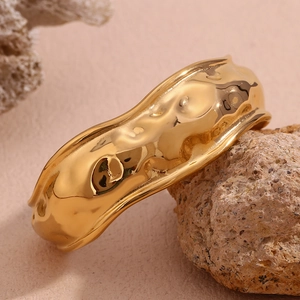 Macro view of wide gold-plated cuff featuring unique molten lava texture on natural stone