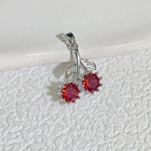 Detail view of a cherry pendant with red faceted crystals and zircon leaf on white surface