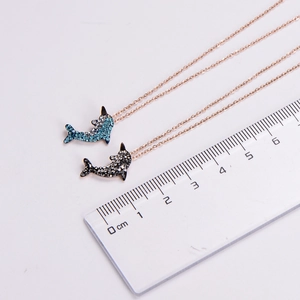 Detailed view of dolphin pendants in blue and black zircon on rose gold chains with scale