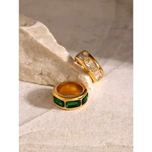 Minimalist wide gold titanium ring with green and clear zircon stones on stone background