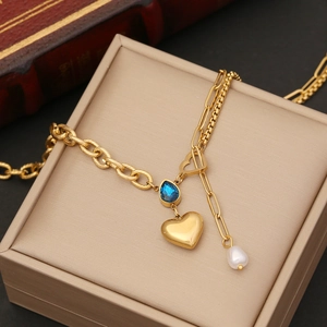 Golden heart necklace with blue gemstone and pearl detail on jewelry box