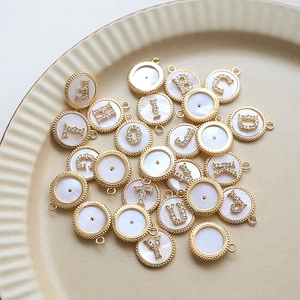 Detail view of gold-plated shell alphabet pendants with zircon inlay on ceramic tray