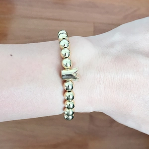 Close-up of a gold-toned beaded bracelet featuring a crown charm on a person's wrist
