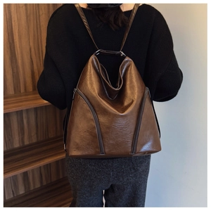 Rear view of a stylish brown leather backpack worn by a model in a minimalist urban setting
