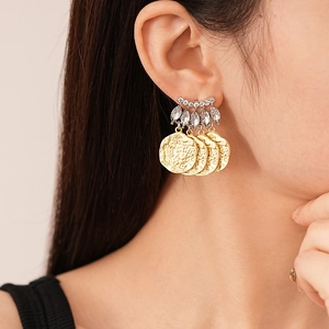 Détail de puce d'oreille argentée avec strass et trois glands de pièces d'or sur modèle