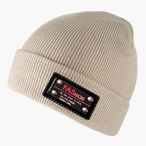 Beige knit beanie with a black leather fashion patch and metal rivets on plain background