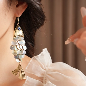 Macro shot of vintage fish drop earring with iridescent shell scales and blue gem eye