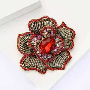 Vintage gold alloy flower brooch with red rhinestones and crystal center on white stand