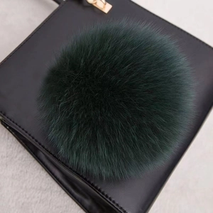 Détail d'un pompon en fourrure vert foncé sur un sac à main en cuir noir mat