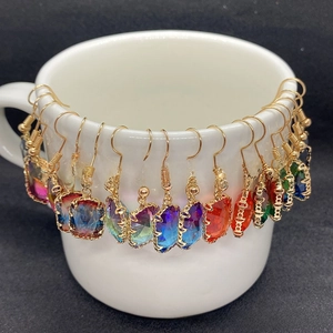 Detailed view of faceted gemstone earrings in various colors on a white ceramic display