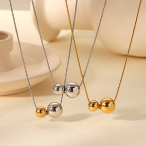 Trois colliers minimalistes bicolores avec pendentif boule sur chaînes serpent sur un vase