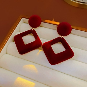 Détail de boucles d'oreilles géométriques en velours bordeaux dans un coffret à bijoux