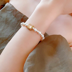 Close-up of a 18k gold plated pearl necklace with a square cat-eye stone on a woman's wrist