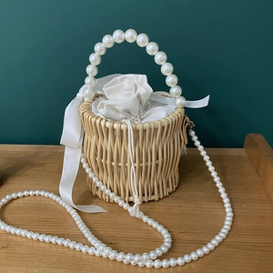 Detail of woven rattan bucket bag with pearl handle and white ribbon bow closure