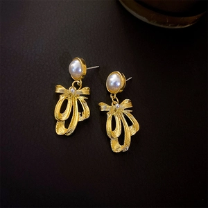Close-up of vintage pearl earrings with gold bow accents on dark leather background