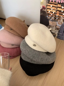 Close-up of colorful wool berets stacked on wood table with metal JM logo detail