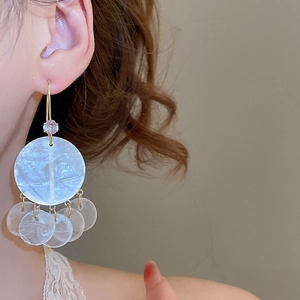 Macro detail of geometric round shell tassel earrings with zircon studs on a model