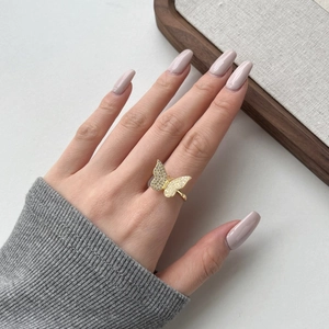 Close-up of a golden butterfly ring with sparkling zircon stones on a model's finger