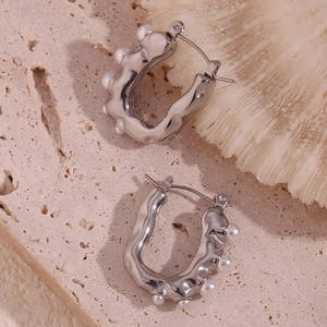 Macro detail of silver U-shaped earrings with wave patterns and white pearl embellishments