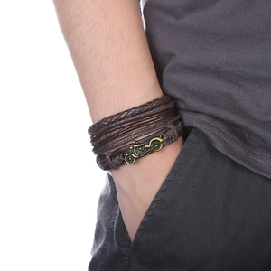 Détail d'un bracelet multicouche en cuir tressé marron avec breloque moto vintage au poignet